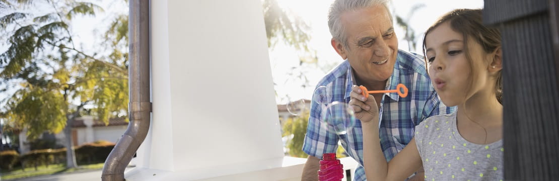 Elderly man and young girl blow bubbles together on a porch